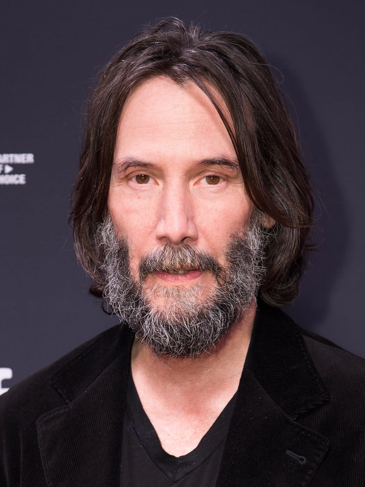 Frontal prestige crop — black mid-length, salt-and-pepper beard, calm dark gaze under festival key.